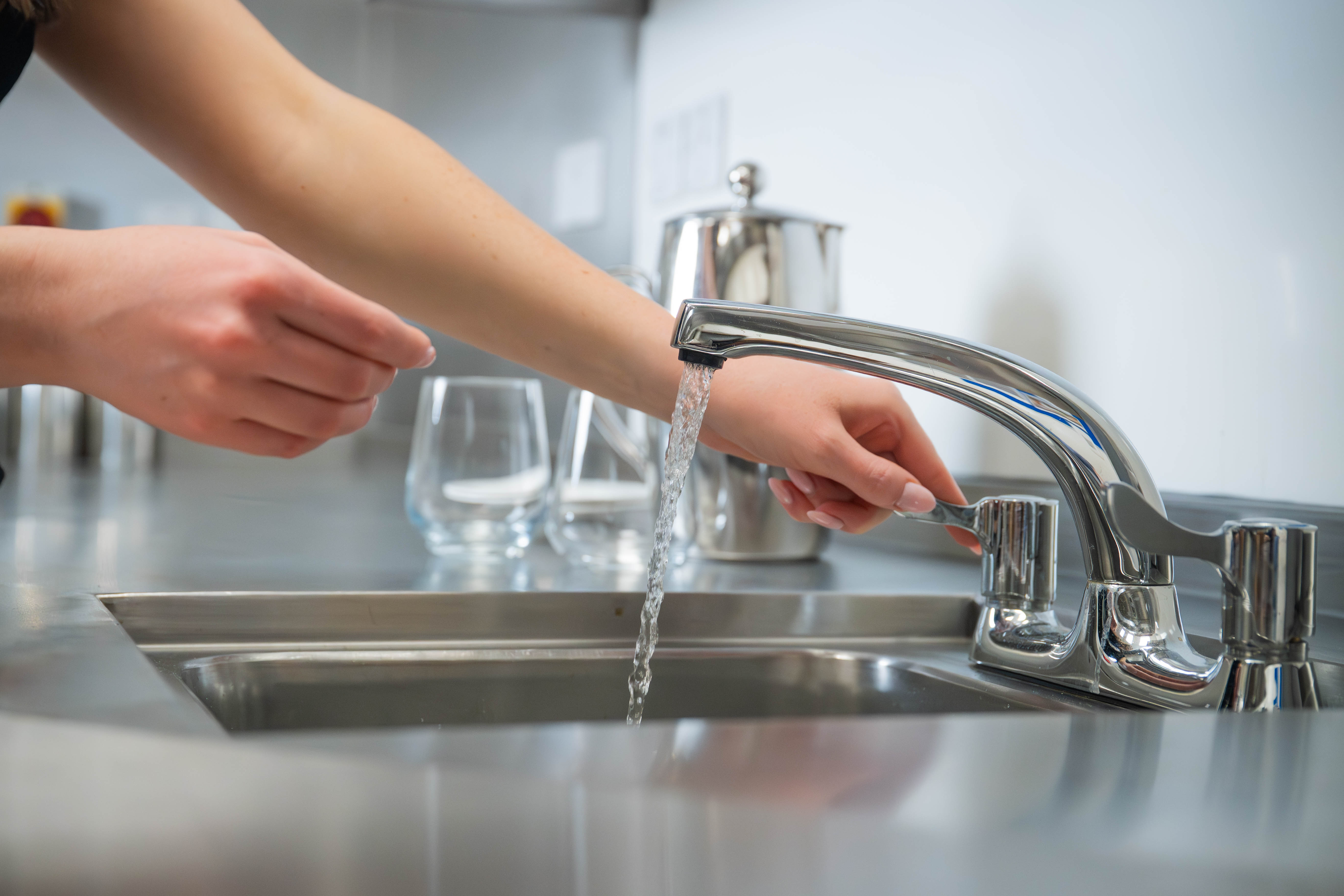 Close-up of woman's arms and hands as she operates tap at commercial sink