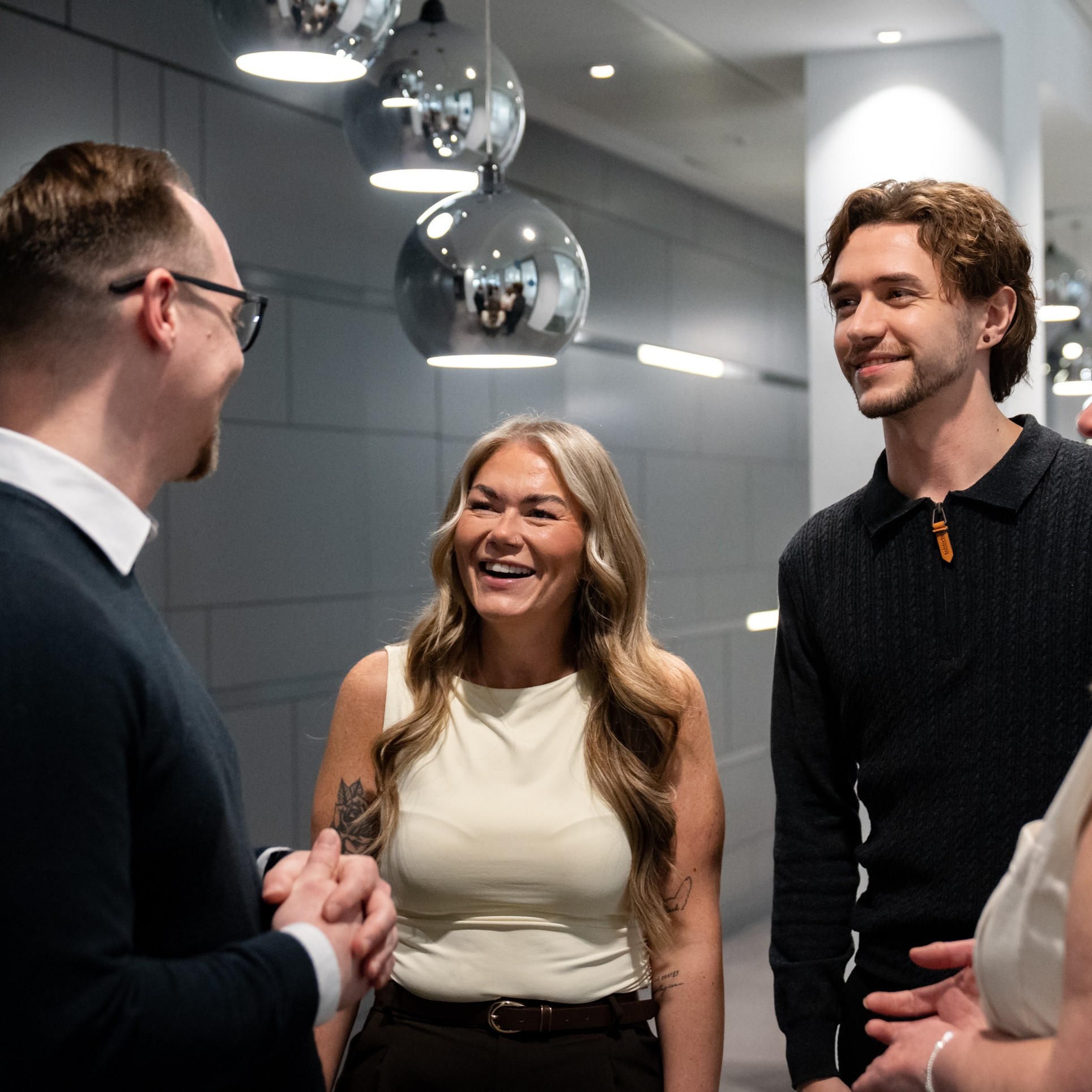 A woman and two men standing smiling and chatting against a dark grey background