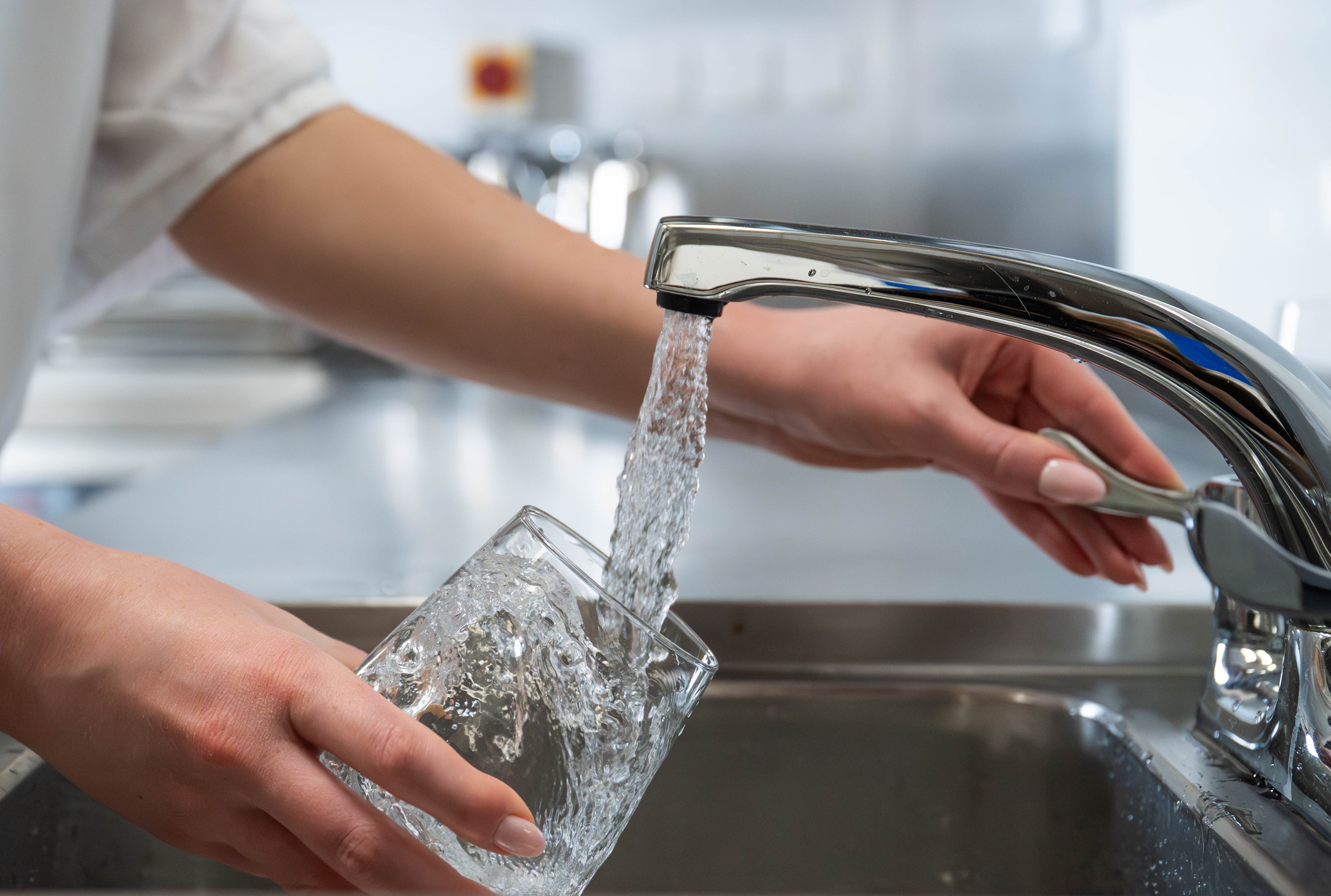 Close-up of water flowing from tap into a glass in a commercial kitchen with female hands visible
