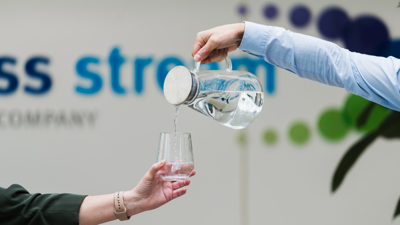 Water being poured from a glass jug into a glass held by another person