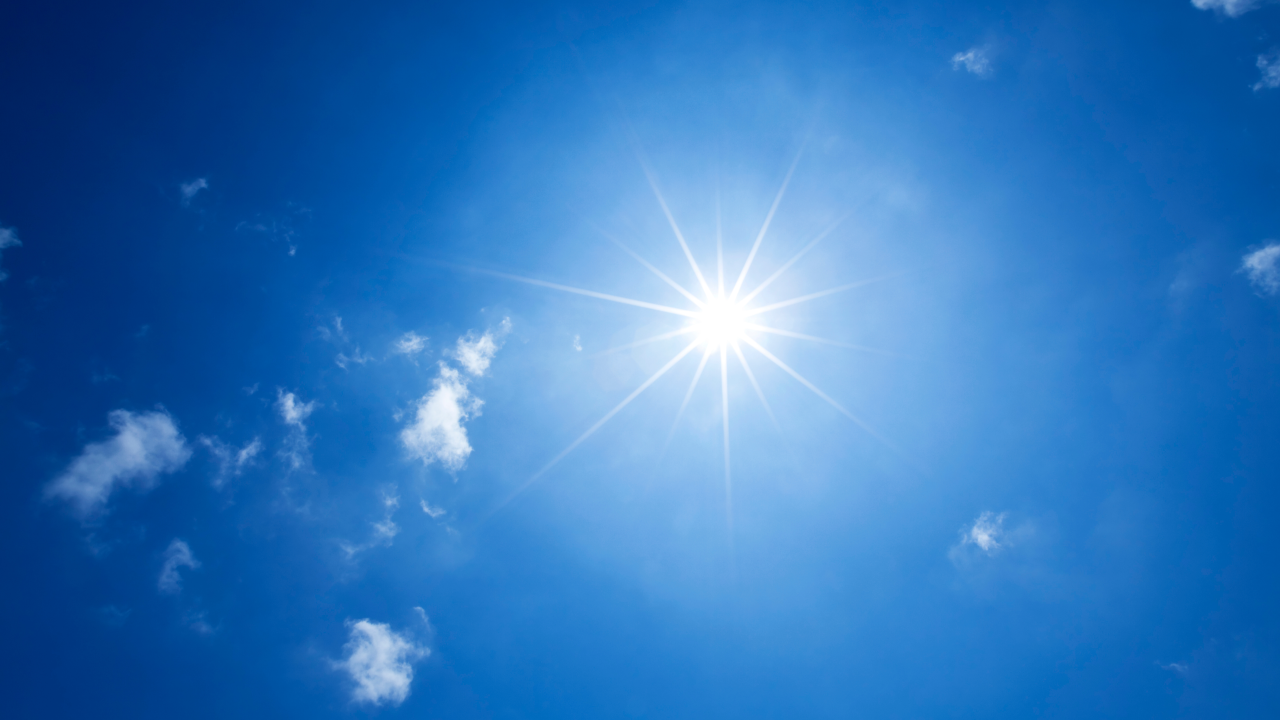 Bright sun shining in a clear blue sky with scattered clouds.