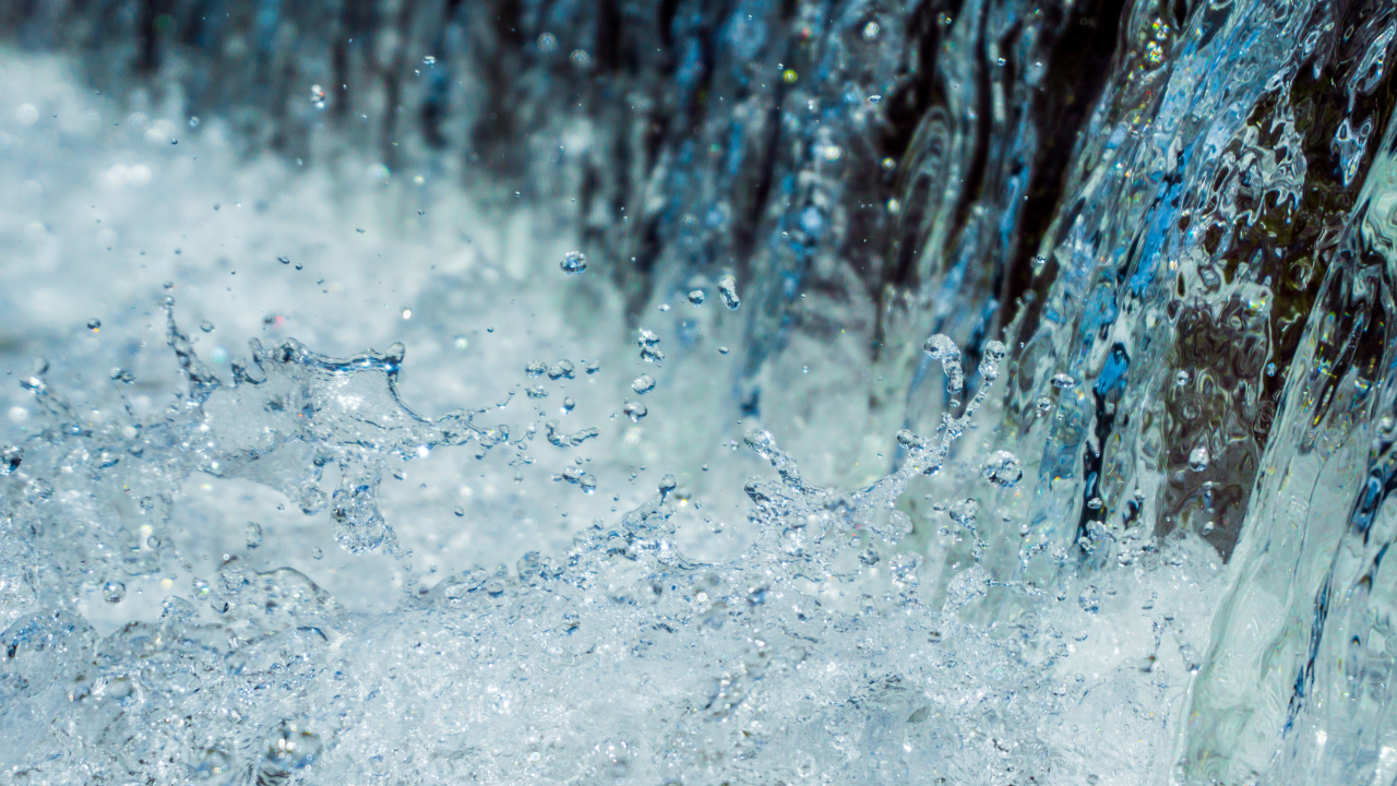A close-up image of water cascading down a waterfall with splashes and droplets captured in mid-air. The water appears clear and blue.