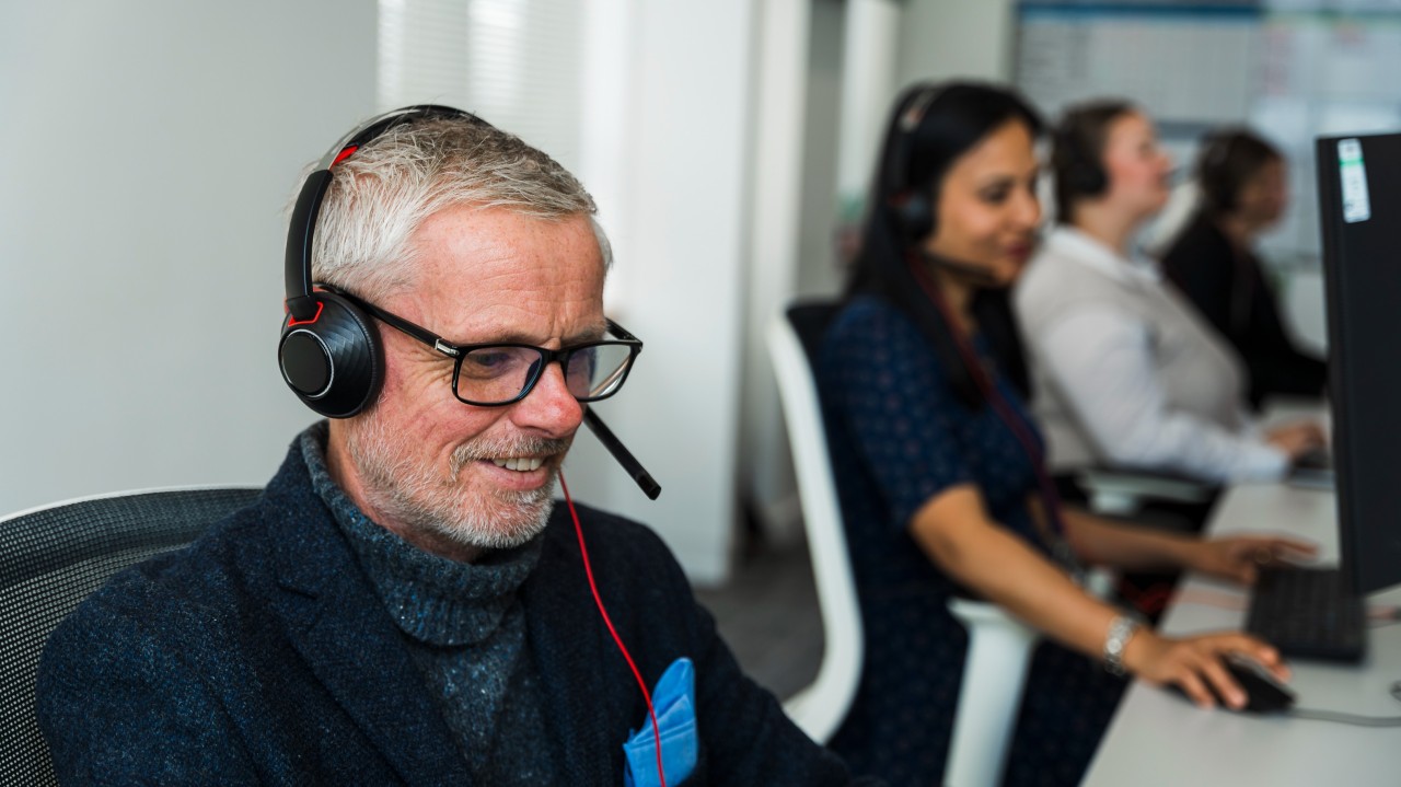 Four people wearing headsets work at computers in a bright office.