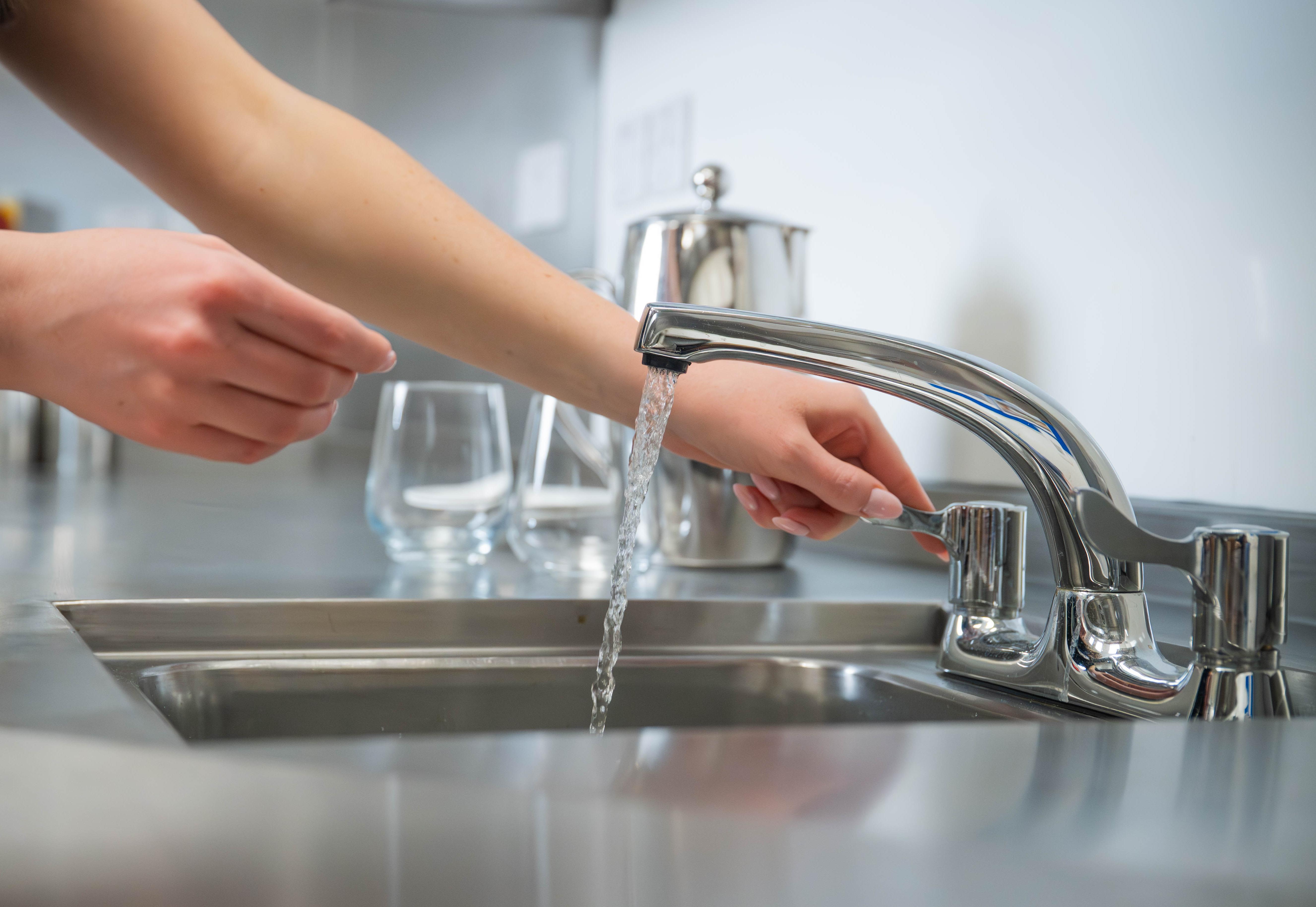 Close-up of woman's arms and hands as she operates tap at commercial sink
