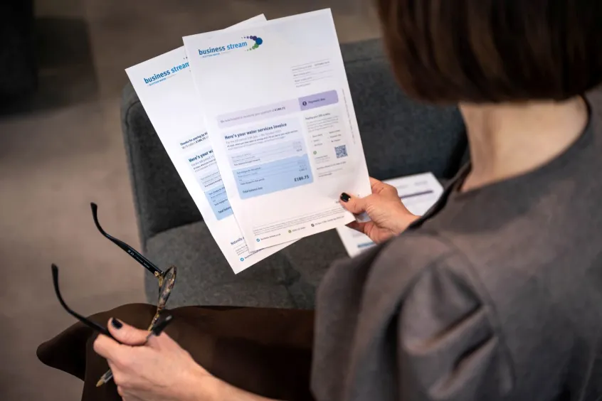 Over the shoulder of a woman reading a water bill and holding a pair of glasses