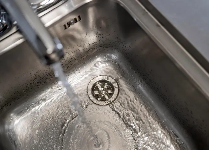 A running tap, with water flowing into an empty, metallic sink