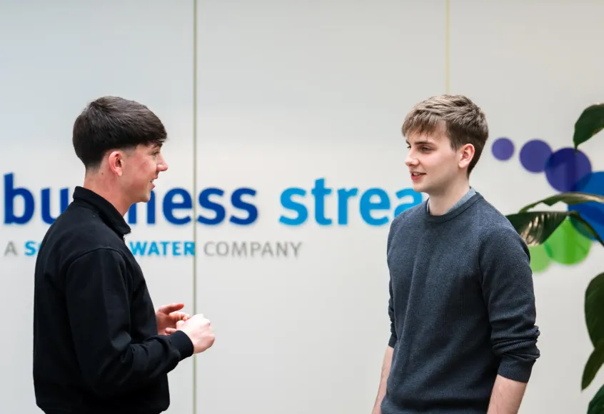 Two young men talking in front of Business Stream logo
