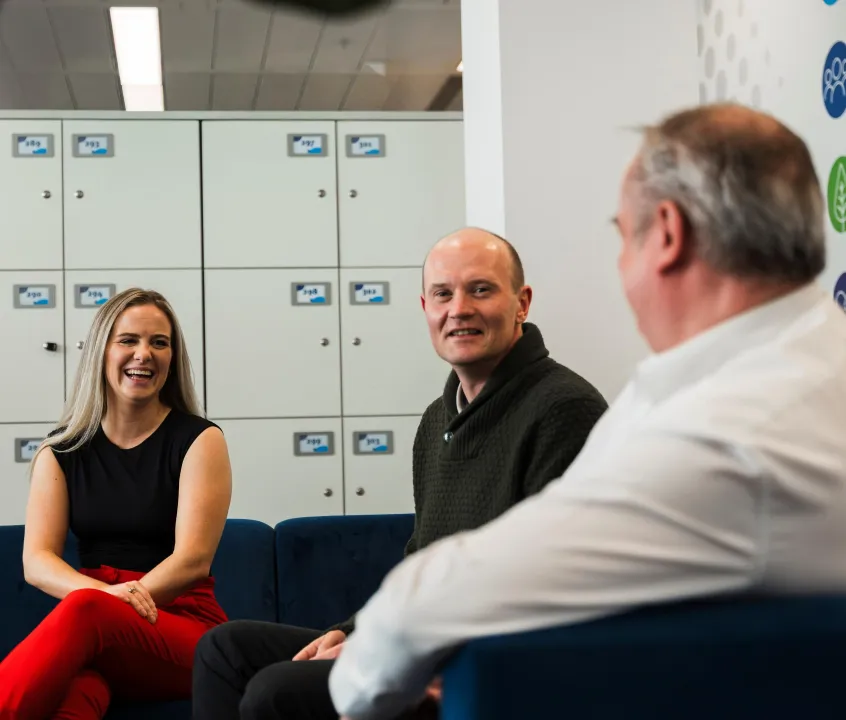 Woman and two men relaxing and chatting on sofas in an office breakout space