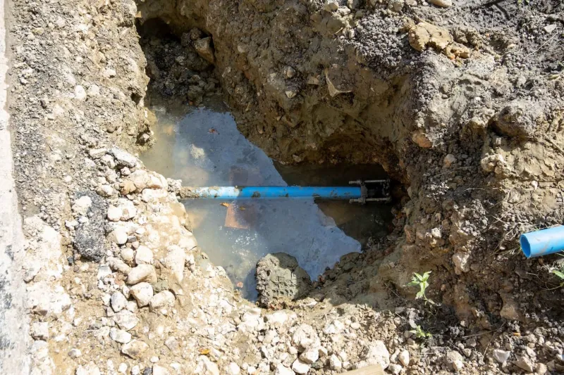 Hole in ground showing leaking external water pipe in pool of water