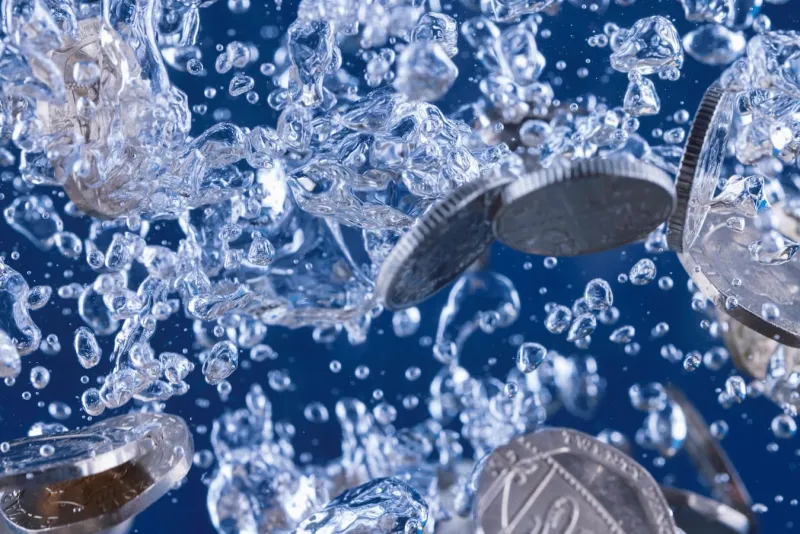 Silver coins falling through water surrounded by bubbles against a blue background