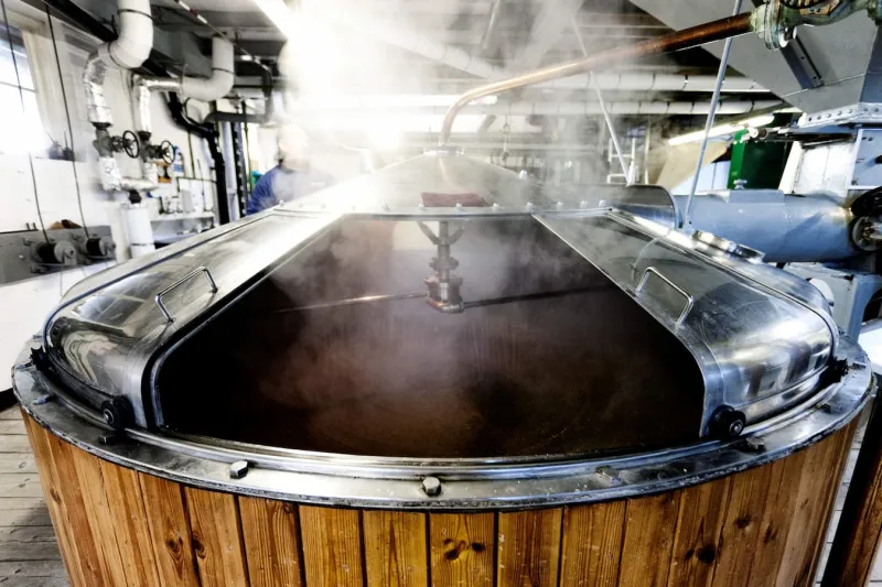 Large wooden brewery vat with steam rising from a large opening and stirring arms visible within