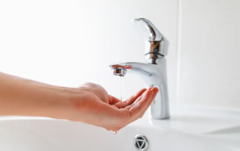 Woman's hand beneath a trickling tap in a bathroom