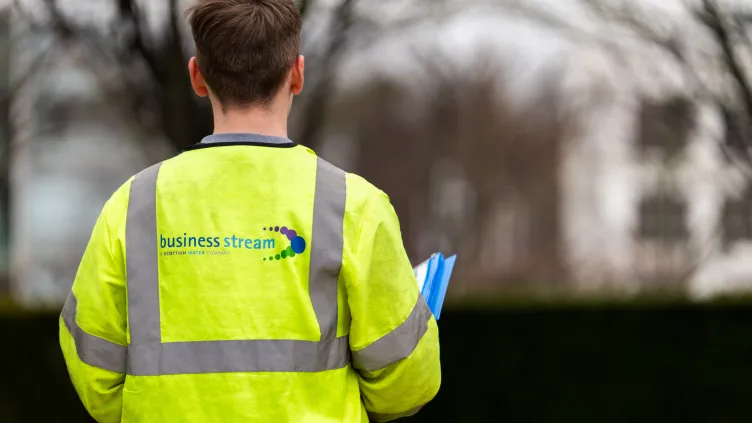 Worker in a high-visibility Business Stream jacket, seen from behind holding a clipboard outdoors