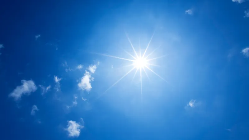 Bright sun shining in a clear blue sky with scattered clouds.