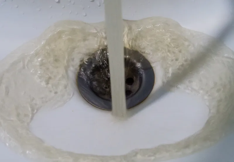 Discoloured water flowing from a tap into a white sink