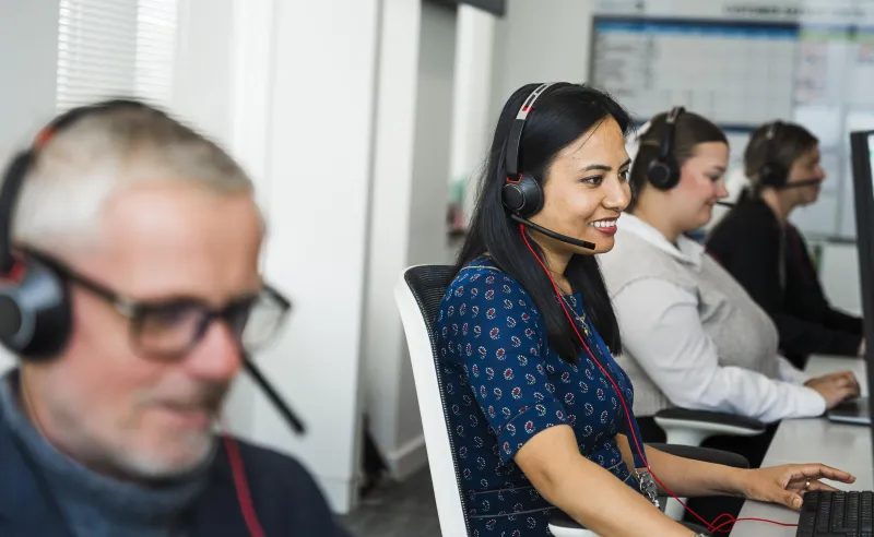 Three women and a man wearing headsets and smiling in a customer service setting