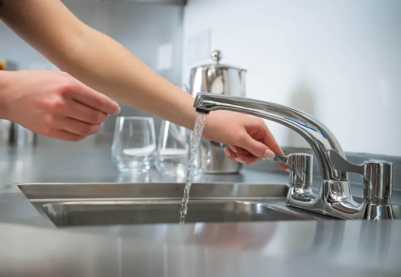Close-up of woman's arms and hands as she operates tap at commercial sink