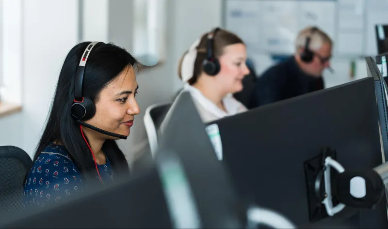 Two women and a man wearing headsets in a customer service setting