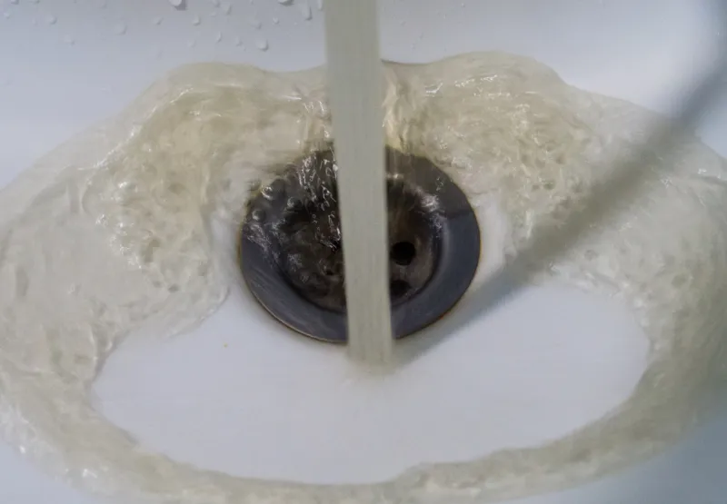 Discoloured water flowing from a tap into a white sink